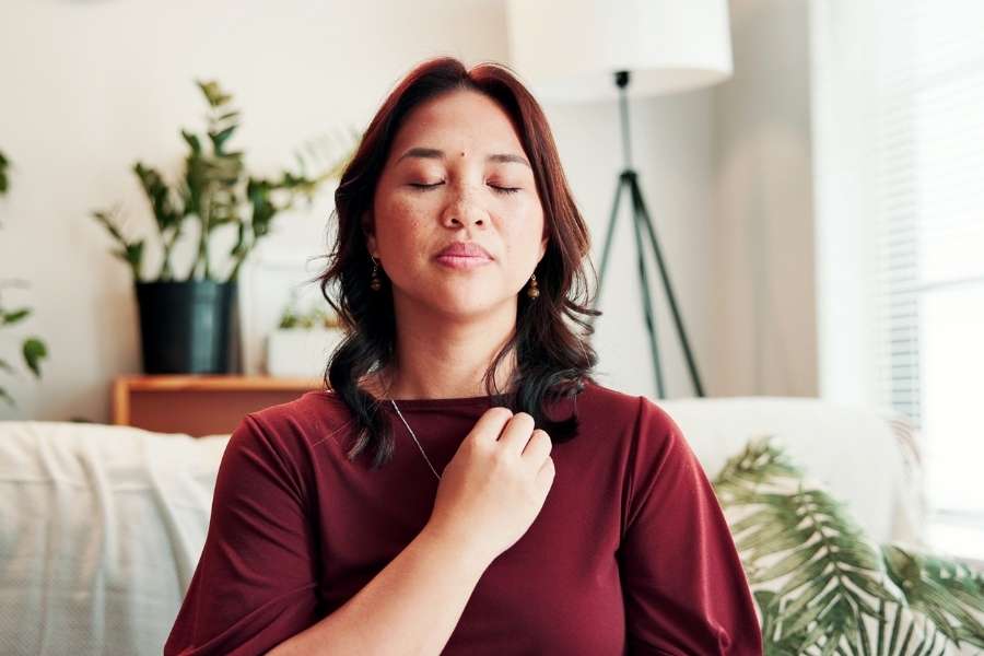 Une femme en haut bordeaux médite les yeux fermés, la main sur la poitrine, illustrant des techniques de respiration apaisantes.