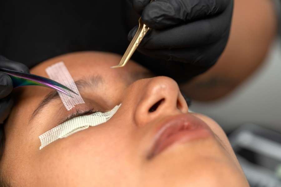 Une esthéticienne en gants noirs applique des extensions pour sublimer des yeux verts.